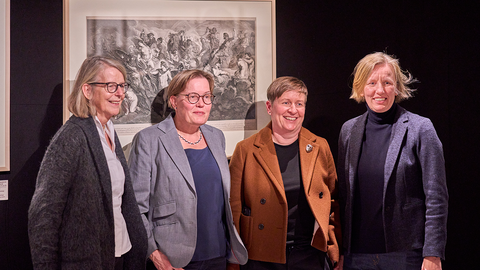 Gruppenbild von (v.l.n.r.) Prof.in Dr. Gerok-Reiter, Prof.in Anja Wolkenhauer, Dr. Ariane Koller und Prof.in Anna Pawlak vor einem gerahmten hellen Druck vor dunklem Hintergrund