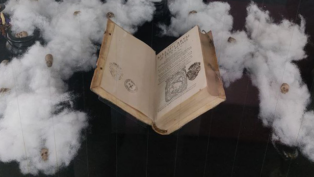 Nachdruck des Hexenhammers Malleum Maleficarum Kleinformatiges aufgeschlagenes Buch auf schwarzem Untergrund, umrahmt von weißer Watte mit kleinen Dekoschädeln darin