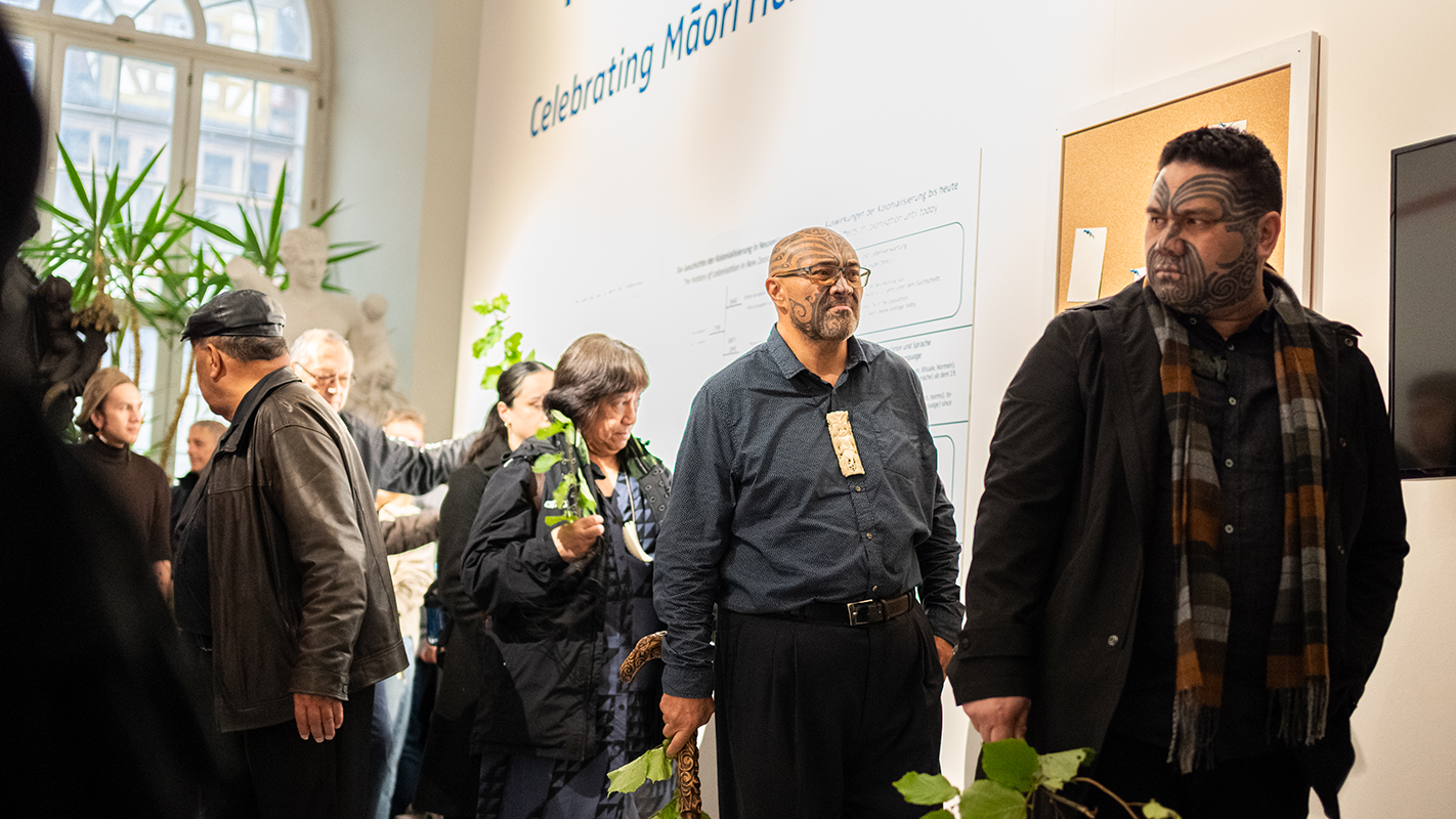 Teilnehmende Maori der Prozession während der Zeremonie vor einer der Ausstellungswände, mit begrünten Zweigen in den Händen