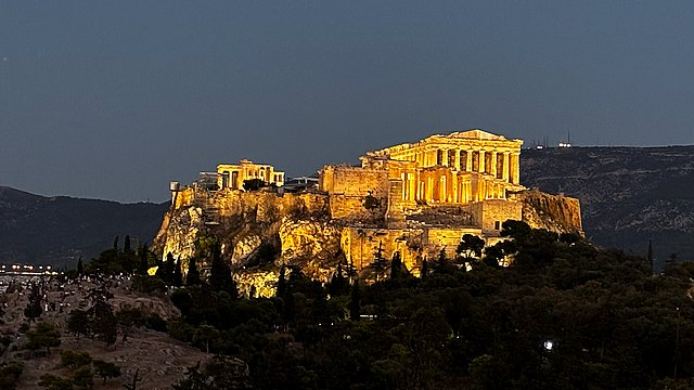 Nächtlich beleuchtete Ansicht des Aufstiegs zur Athener Akropolis im Kontrast zur dunklen Umgebung
