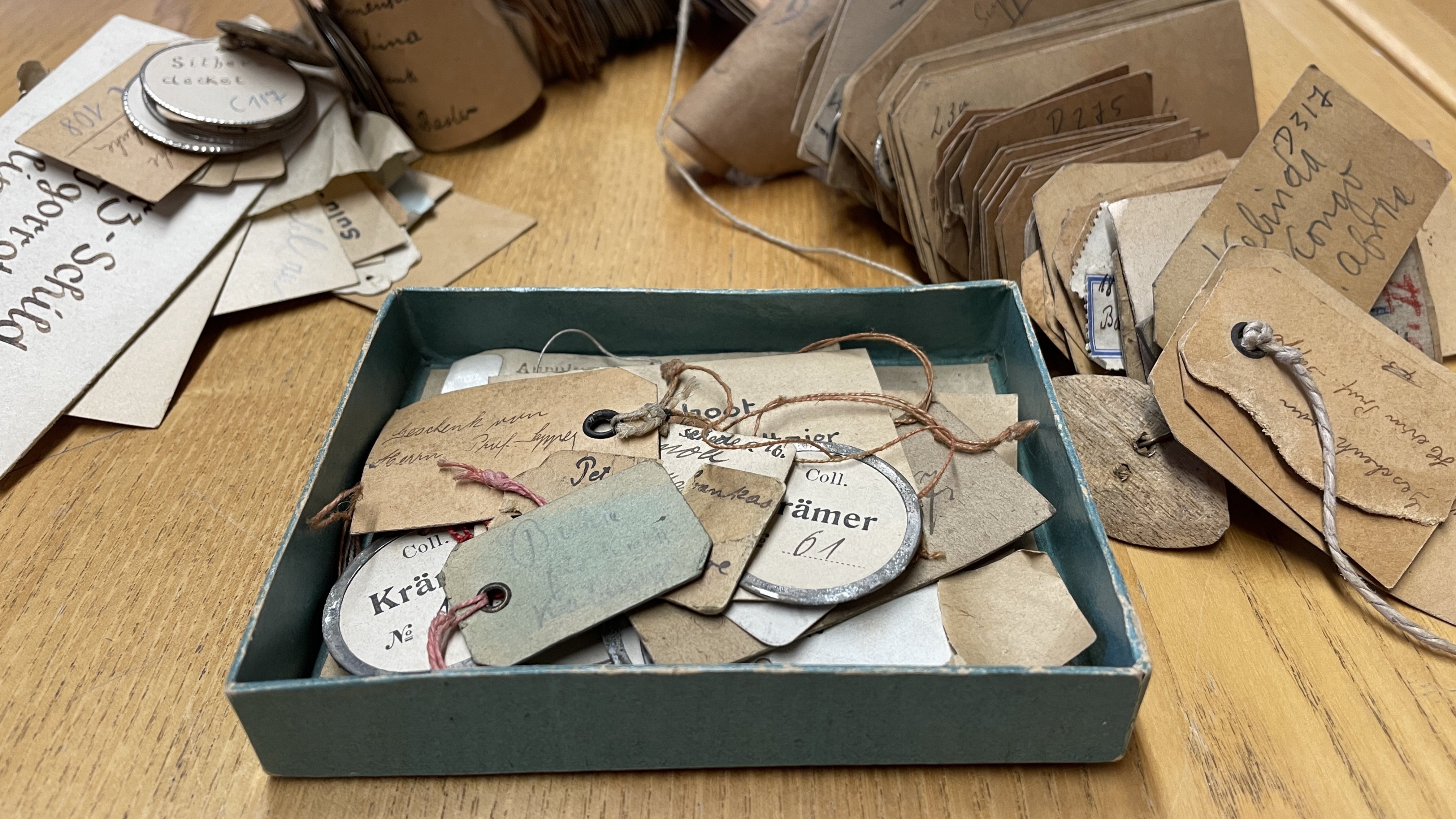 Aufgefädelte historische Etiketten um eine Box mit losen historischen Etiketten, alle bedruckt oder handschriftlich beschrieben