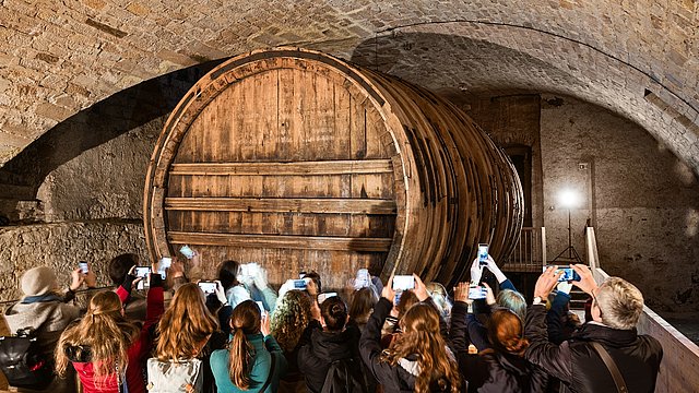 In einem Gewölbekeller des Schlosses Hohentübingen steht eine Gruppe von Menschen und fotografiert ein Riesenweinfass