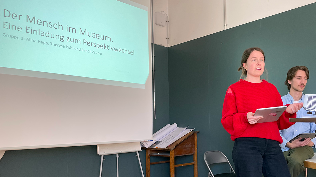 Alina Happ im Vortrag vor einer auf die Leinwand projizierte Folie mit der Folie "