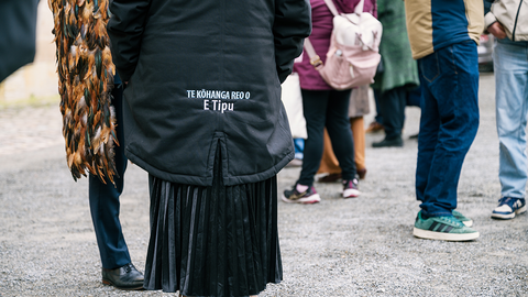Leute auf dem Schlosshof, Rückansicht einer Jacke mit der aufgestickten Aufschrift "Te Kohanga Reo o/E Tipu"