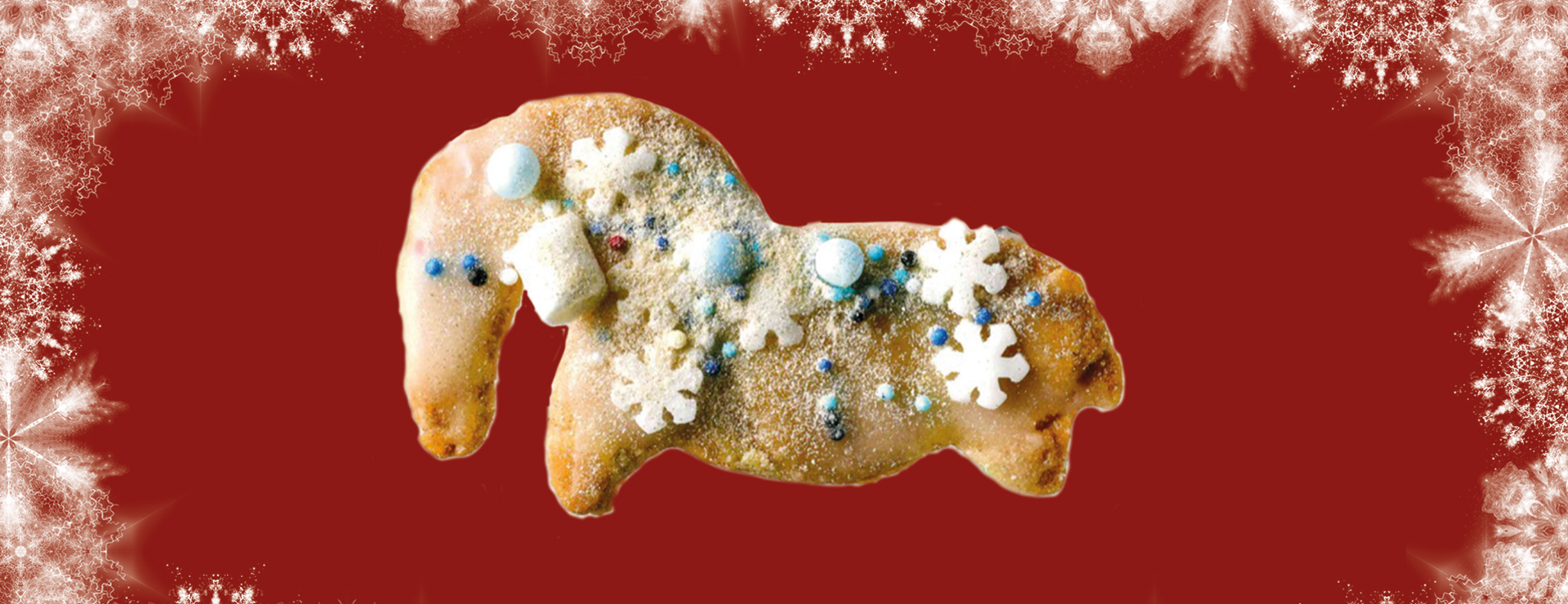 Keks in Form des Urzeitpferdchens, dekoriert mit Zuckerschneeflocken und Minimarshmallows, vor rotem Hintergrund und umrahmt von weißen Schneeflockenmotiven