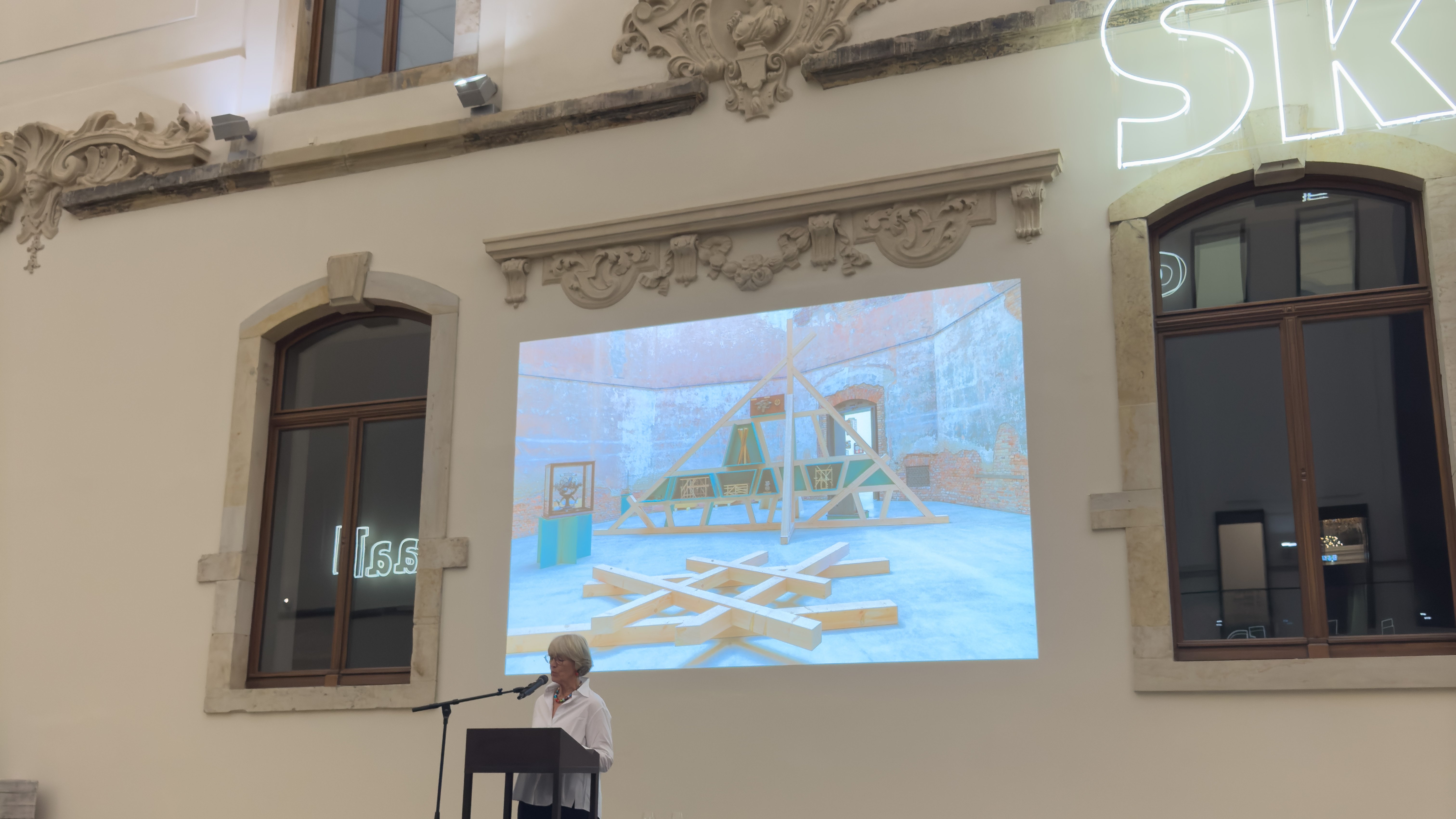 Zu sehen ist eine ältere Frau am Pult mit eröffenden Worten bei der Ausstellungseröffnung zur Ausstellung 