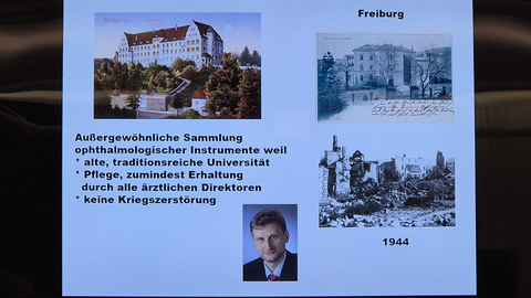 Aufnahme einer Bildschirmpräsentation mit Bildern des Gebäudes der Alten Augenklinik, einem erklärenden Text zu den Alleinstellungsmerkmalen der Sammlung ophthalmologischer Instrumente, die mangels Kriegszerstörung gut erhalten ist, und unten das Portrait eines blonden Manns im Anzug
