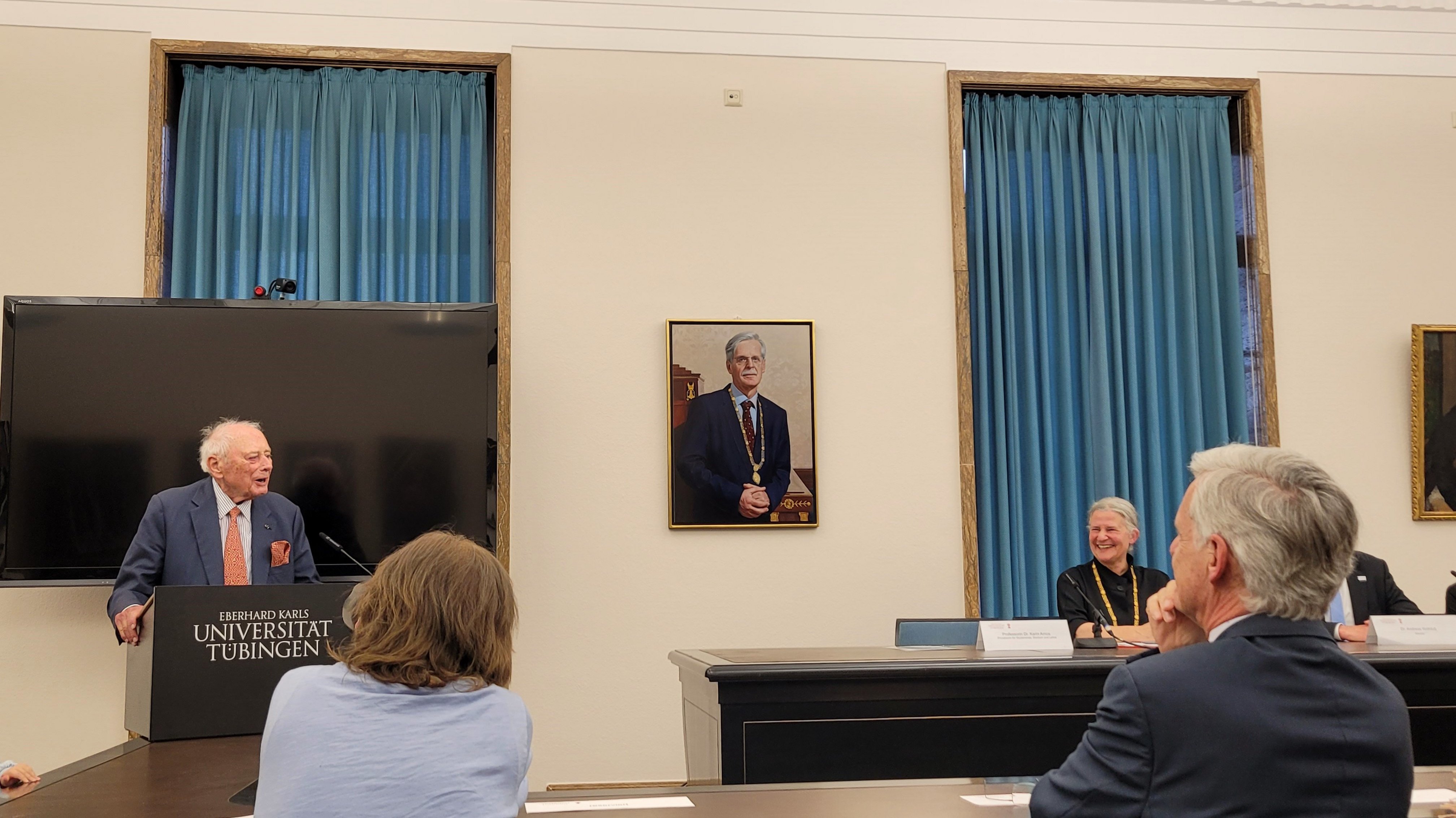 Personen in Rückansicht blicken auf Herrn Würth am Rednerpult, in der Mitte des Fotos hängt ein Portrait von Bernd Engler an der Wand