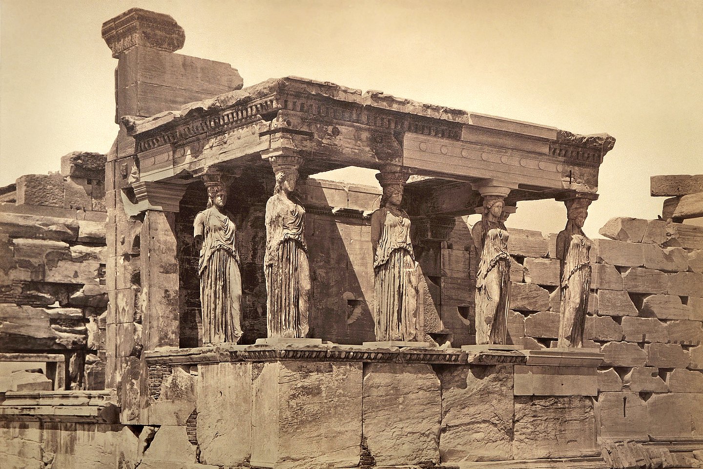 a sepia-toned photo of the ruins of an open hall with female statues as columns
