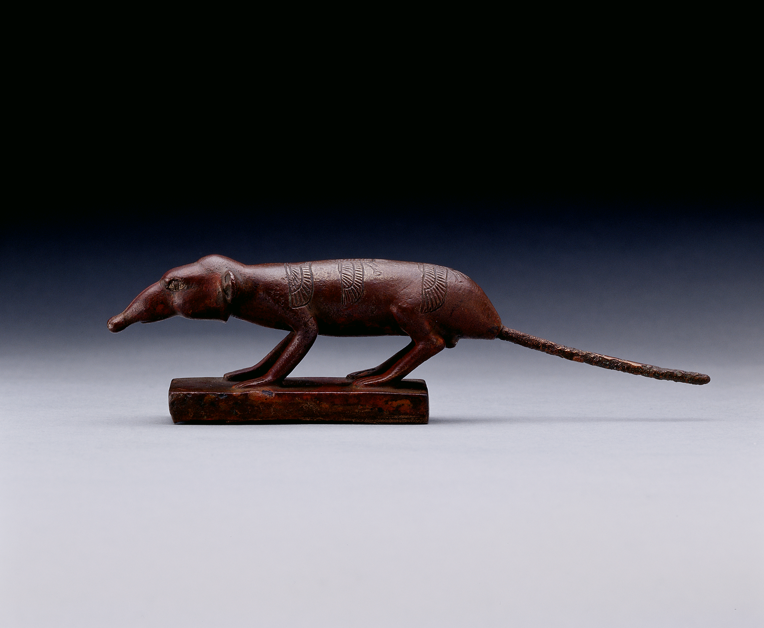 Bronzene Statuette einer nach links gewandten, mit Flügelmustern verzierten Spitzmaus auf einer rechteckigen Basis vor schwarzem Hintergrund