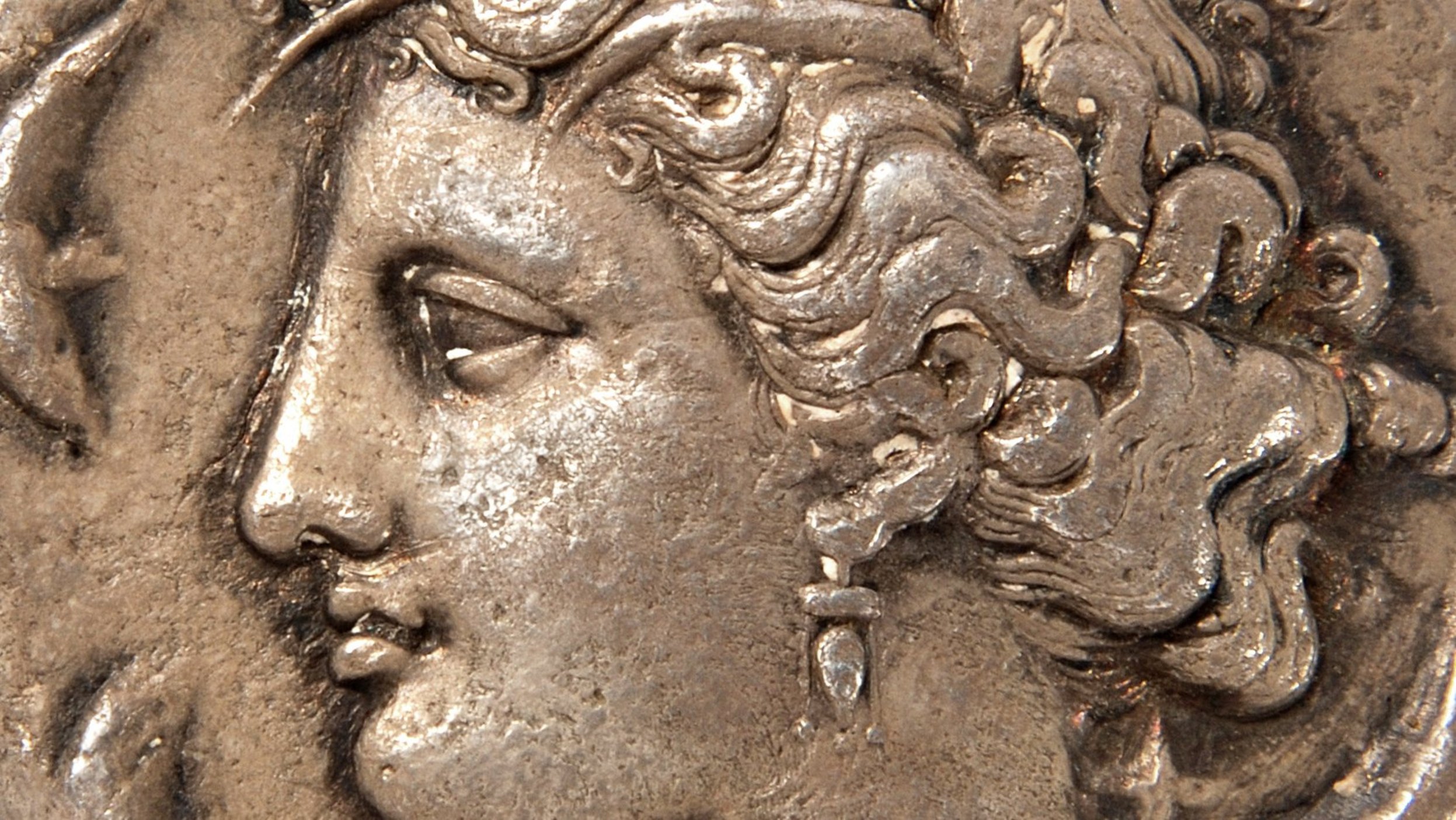 Silver coin with crowned female head looking left, wearing an earring and a vaguely visible necklace; to the left and right are three dolphins, the one on the bottom left is cut off from the head downwards