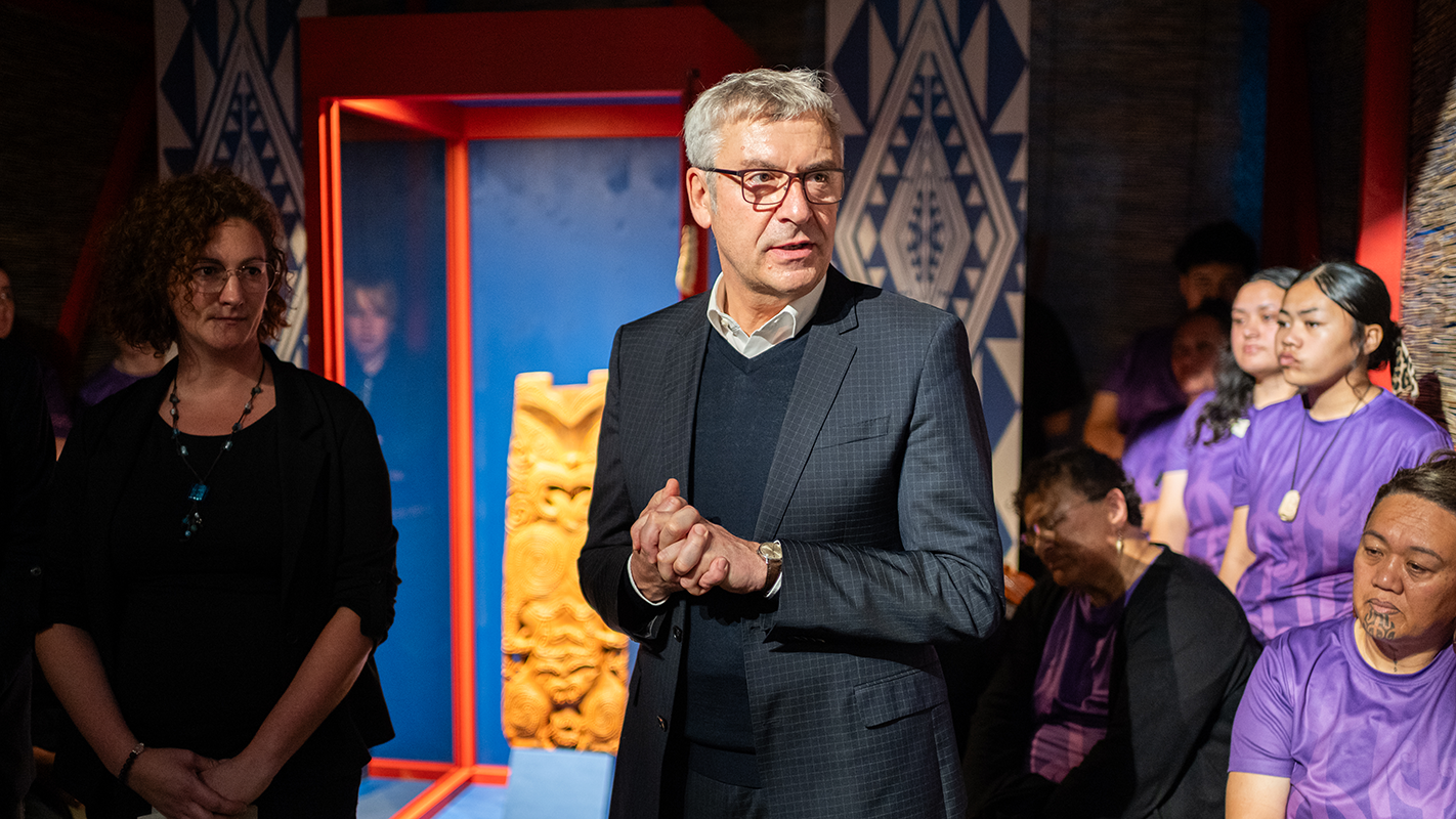 Museumsdirektor Prof. Dr. Ernst Seidl steht sprechend vor einer Vitrine mit dem Schnitzwerk (pou), das die Maori-Anführerin Hinematioro darstellt, links und rechts sind Zuhörende aus der Tübinger und der gastierenden Maori-Delegation