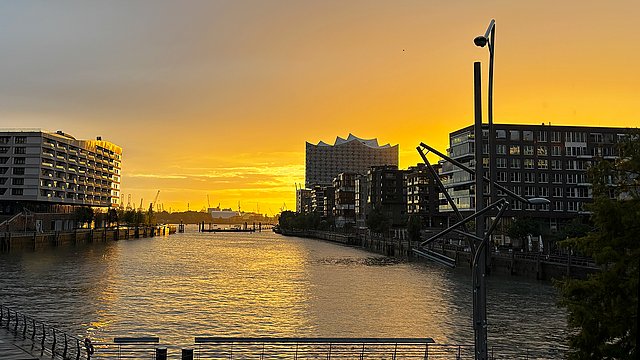 Sonnenuntergang hinter der Hamburger Elbphilharmonie mit Reflektionen auf dem Wasser der Landungsbrücken
