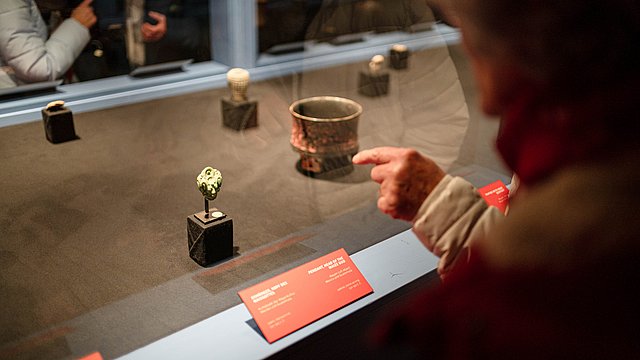 view of the Mayan-blue showcase with the hand of an anonymous visitor in front of the glass indicating a jade head inside