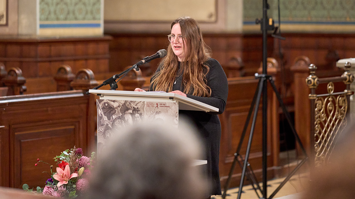 Ida Colangelo am Rednerpult, im Vordergrund die unscharfe Rückansicht der Köpfe der Zuhörenden