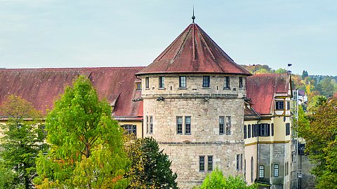 Im Hochformat wird die Westbastion von Schloss Hohentübingen mit weißen Mauern und roten Dächern in spätsommerlicher Begrünung gezeigt.