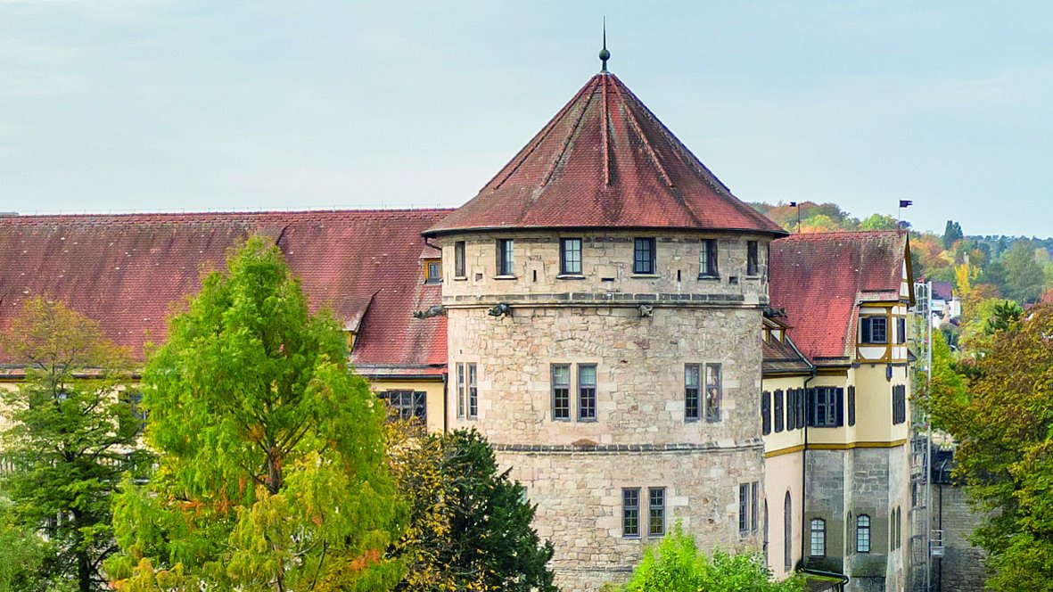 Im Hochformat wird die Westbastion von Schloss Hohentübingen mit weißen Mauern und roten Dächern in spätsommerlicher Begrünung gezeigt.