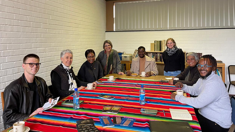 Diskutant*innen des Visual Arts Department der University of Pretoria sitzen um einen Tisch und wenden sich lächelnd der Kamera zu