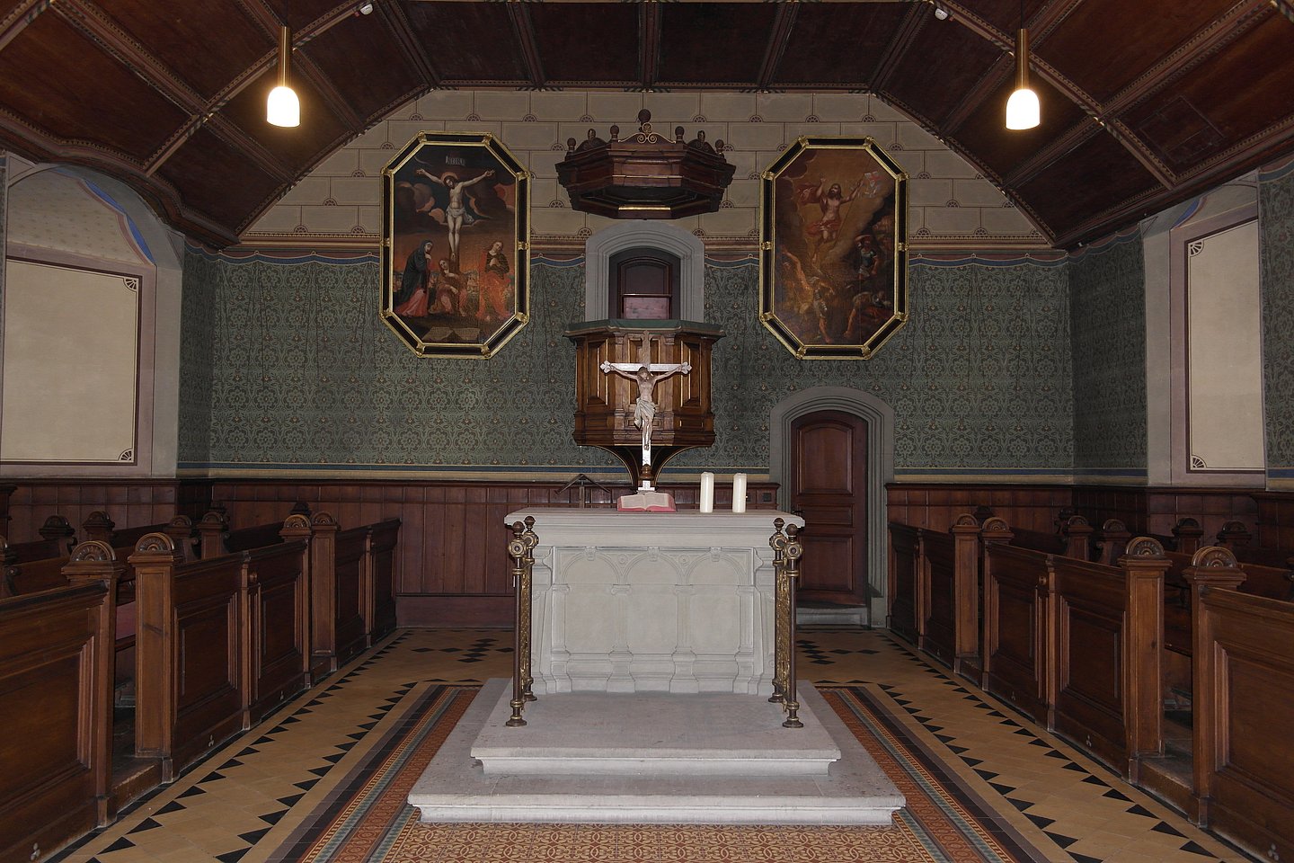 Photo: MUT Frontal view of the altar area of the castle church, with the white altar with the crucified Christus figure upon it; in the background is the pulpit, flanked by tall painting depicting the crucified (left) and ascending (right) Christus respectively