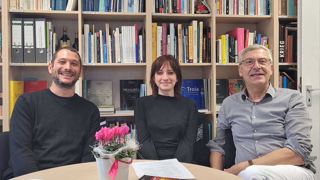 Vor einem Bücherregal sitzen am runden Tisch (v.l.n.r.) Michael La Corte, Tabea Olhorn und Ernst Seidl
