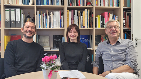 Vor einem Bücherregal sitzen am runden Tisch (v.l.n.r.) Michael La Corte, Tabea Olhorn und Ernst Seidl