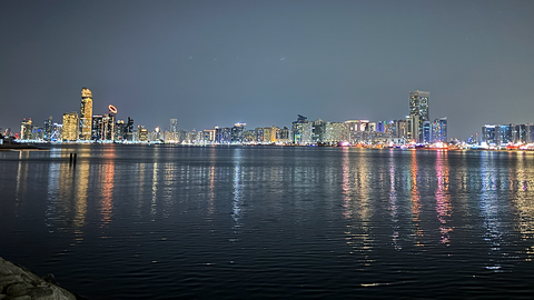 58th Seminar for Arabian Studies, Abu Dhabi Abendliche Skyline von Abu Dhabi mit bunten Reflektionen der beleuchteten Gebäude auf dem Wasser im Vordergrund