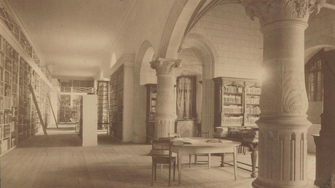 Schwarzweiß-Foto der Universitätsbibliothek im Rittersaal auf Schloss Hohentübingen mit vollen Bücherregalen an den Wänden und einem Arbeitstisch mit Stühlen zwischen den Kolonnaden