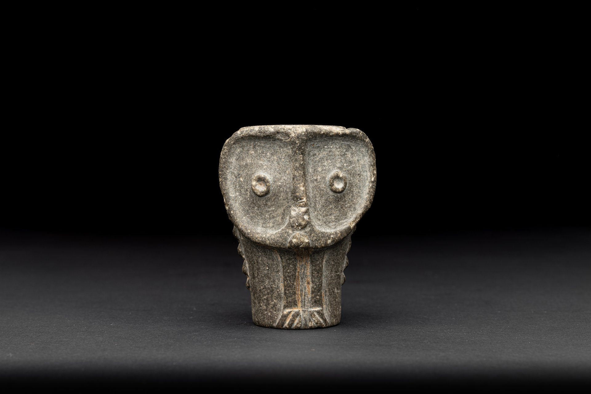 Light grey, compact attachment for a club in the shape of an owl's face against a black background