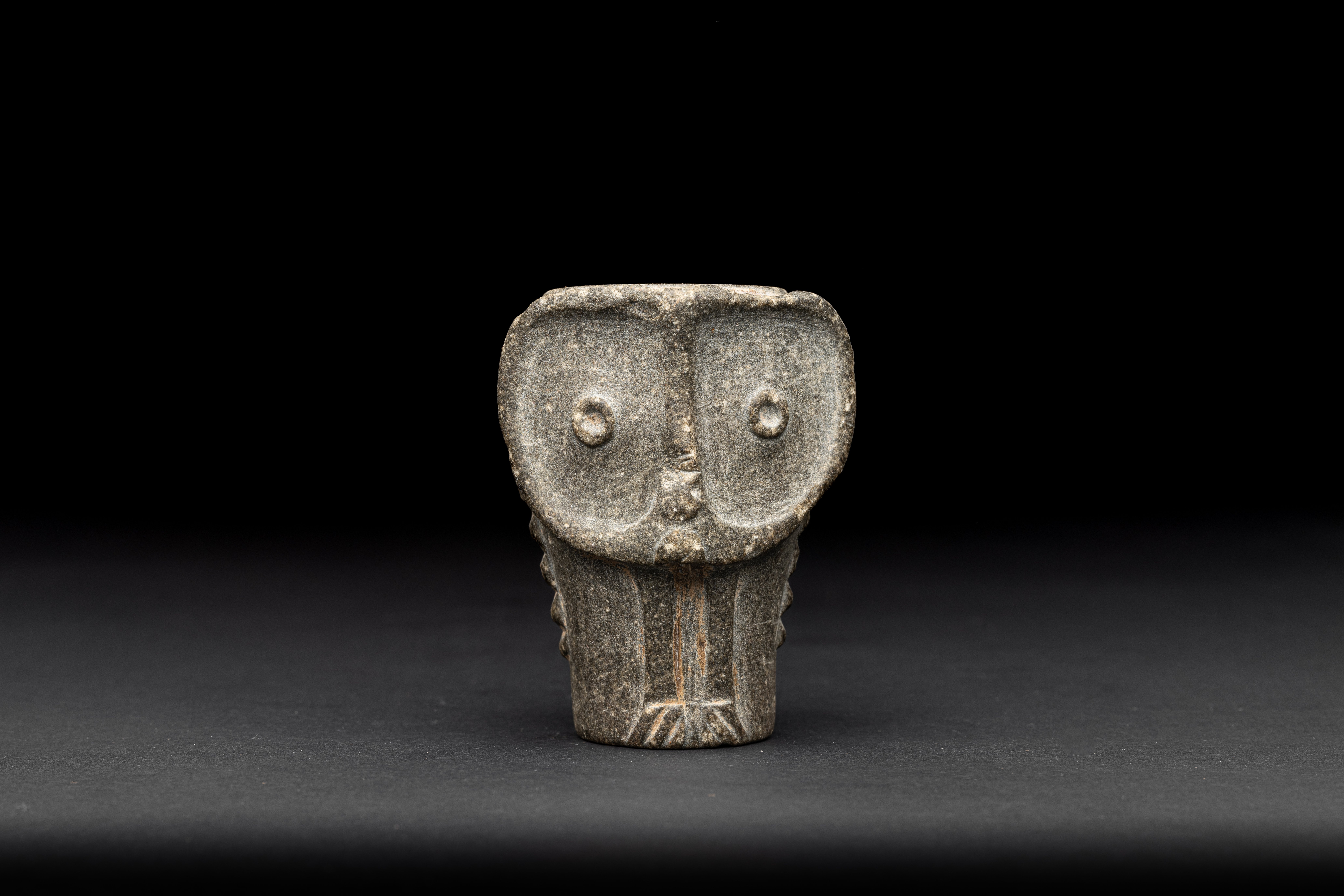 Light grey, compact attachment for a club in the shape of an owl's face against a black background