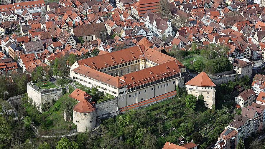 Aereal view of Hohentübingen Castle with greenery over the Castle Hill and the red roofs of Tübingen in the background