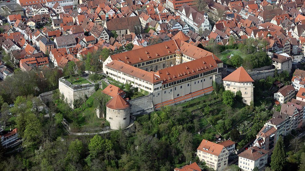 Aereal view of Hohentübingen Castle with greenery over the Castle Hill and the red roofs of Tübingen in the background