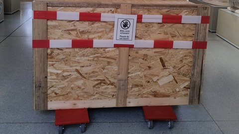 Foto: MUT | Nadja Mozdzen Eine Kiste auf Rollbrettern mit Absperrband umwickelt; ein aufgeklebtes Schild mit einem Handsymbol sagt "Bitte nicht anfassen! Please do not touch!"