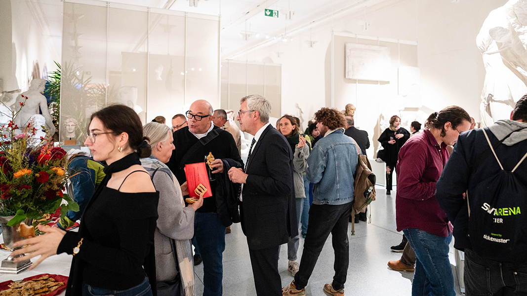 Besuchende haben sich im Rittersaal von Schloss Hohentübingen am Buffet (links) und zwischen den Gipsabgüssen zu Grüppchen versammelt und tauschen sich aus