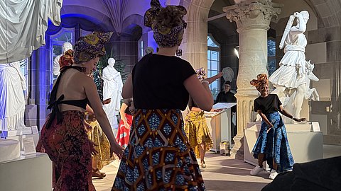 © MUT | Lucas Rau Tanzende Darstellerinnen in farbenfrohen Kleider im Rittersaal von Schloss Hohentübingen bei der Modenschau.