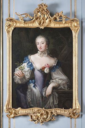 Dreiviertelporträt der Prinzessin Elisabeth Sophie, Gemahlin des Herzogs Carl von Württemberg und Tochter des Markgrafen Friedrich von Brandenburg-Bayreuth. Stehend neben einem Tisch. Linker Ellenbogen aufgestützt, in der rechten Hand blühenden Orangenzweig haltend. Blauviolettes Kleid, Reifrock mit spitzenbesetzter weißer Schürze und glatter Schnürtaille. Im Hintergrund Ausblick in Parklandschaft. Die linke Hand, die jetzt einen Zipfel der Schürze hält, hatte ursprünglich das Ende einer Blumengirlande gefasst, die später übermalt wurde.