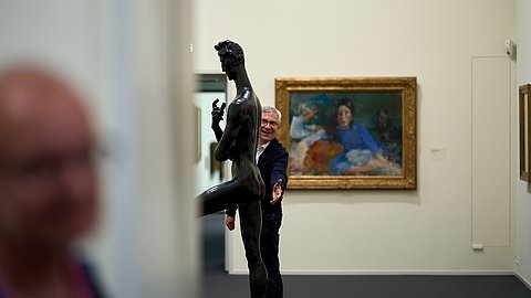 © MUT | Fabian Kurze Zu sehen ist Ernst Seidl mit verschmitztem Grinsen der einer Statue seine Hand vor den Po hältKunsthaus Tübingen