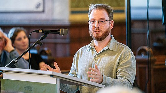 Lucas Rau im graugrünen Leinenhemd steht gestikulierend am Rednerpult
