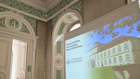 Rechts im Bild Leinwand mit projiziertem Bild des Schlosses Hohenheim, links die Schrift "Wissenschaftliche Sammlungstag Baden-Württemberg" und das Logo der Universität Hohenheim