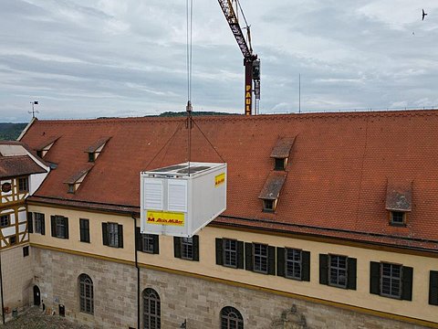 © Hermann Paule GmbH & Co. KG | H. Singer Zu sehen ist ein Kran, der eine Kiste mit Material über das Dach von Schloss Hohentübingen hebt