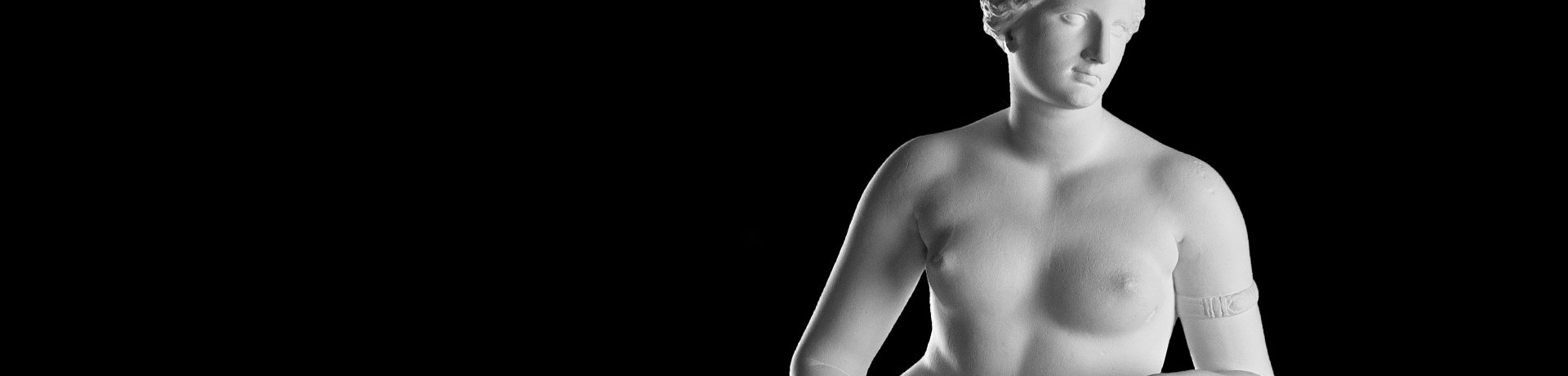 Büsten-Ausschnitt einer weißen Statue einer unbekleideten Aphrodite mit nach rechts geneigtem Kopf und einem Reifen an ihrem linken Arm
