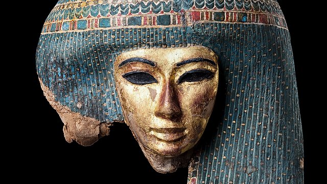 Photo: MUT | Valentin Marquardt Coloured Egyptian mummy mask with elaborately decorated pearl hairstyle against black background