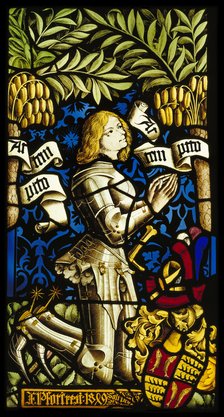 Farbenfrohes Glasfenster mit einer mittelalterlichen Darstellung. Zu sehen ist ein kniender Ritter in silberner Rüstung mit blonden Haaren, der die Hände zum Gebet gefaltet hat. Um ihn herum sind dekorative grüne Blätter und goldene Trauben zu sehen. Neben ihm liegt ein Helm mit rot-schwarzem Wappen. Ein Schriftband mit lateinischem Text windet sich durch das Bild.