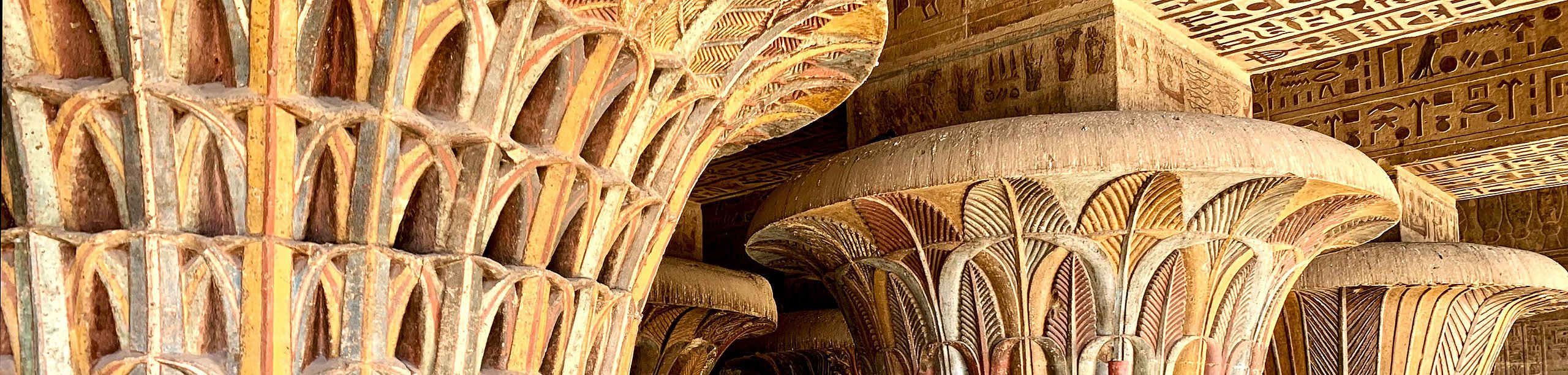 In Beige- und Rottönen gefasste Säulenkapitelle mit Fluchtpunkt rechts im Bild, darüber Deckenbalken mit Hieroglyphen