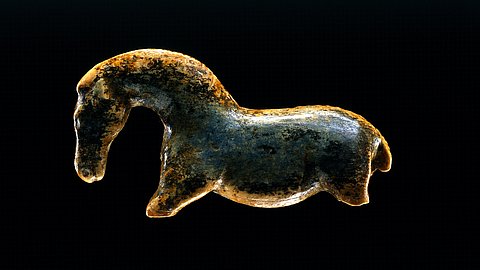 Nach links gewandte Wildpferdfigurine aus Elfenbeinmarmor mit gewölbtem Hals vor schwarzem Hintergrund