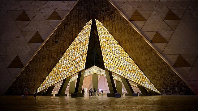 Erleuchteter Museumseingang bei Nacht. Der Eingang hat eine pyramidale Form.