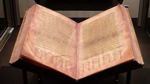Foto: Universitätsbibliothek Tübingen In einer Vitrine aufgeschlagenes Buch auf schwarzem Grund; die Seiten des Codex Argenteus sind mit Silberfarbe beschrieben
