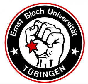 Rundes Logo mit schwarzem Hintergrund und rotem Rand. In der Mitte ist eine erhobene Faust mit einem roten Stern auf dem Handrücken. Im äußeren Ring steht in weißer Schrift ‚Ernst Bloch Universität Tübingen‘, getrennt durch zwei weiße Sterne.