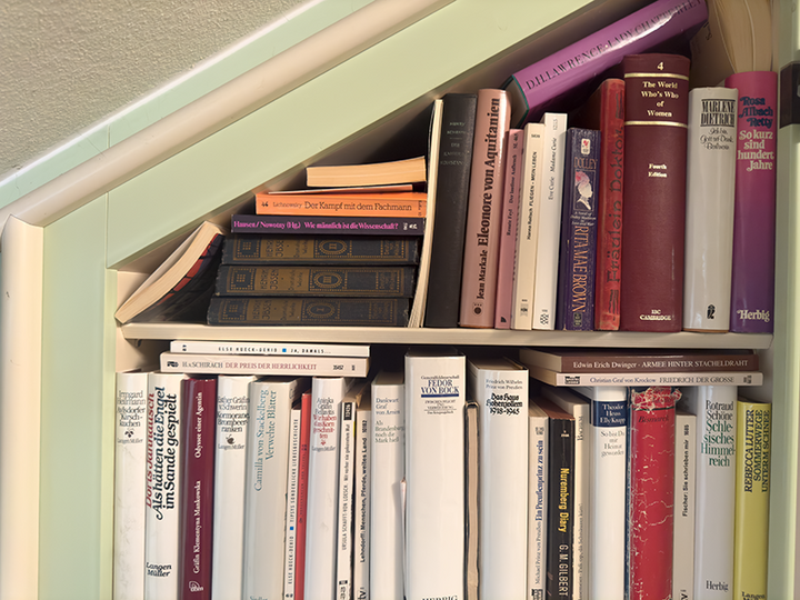 Section of a built-in bookcase with the sloping, painted mint-green, to the left; filled with novels with white, red and dark-coloured spines