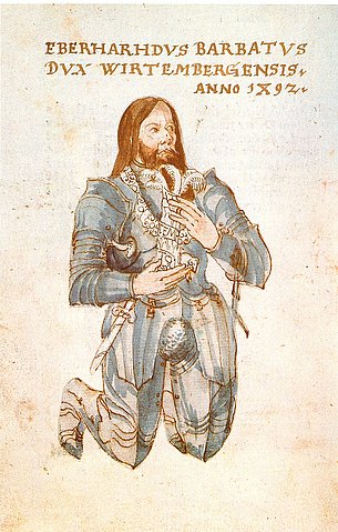 Eine historische Illustration zeigt einen bärtigen Mann in einem detaillierten Ritterharnisch, der auf einem Knie kniet. Seine Hände sind zum Gebet gefaltet, sein Blick ist andächtig nach oben gerichtet. Über ihm befindet sich eine lateinische Inschrift. Der Hintergrund ist schlicht und hell, wodurch die Figur im Vordergrund hervorgehoben wird.