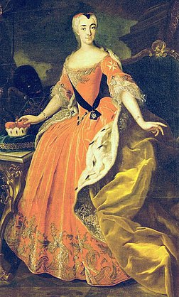 Porträt einer Frau aus dem 18. Jahrhundert in einem prunkvollen, orangefarbenen Kleid mit goldenen Stickereien und einer weißen, pelzverzierten Schleppe. Sie trägt eine hochgesteckte Frisur und hält in der linken Hand ein Tablett mit einer Kuchenstück. Der Hintergrund zeigt Möbel und dunkle Vorhänge, die die elegante Atmosphäre unterstreichen.